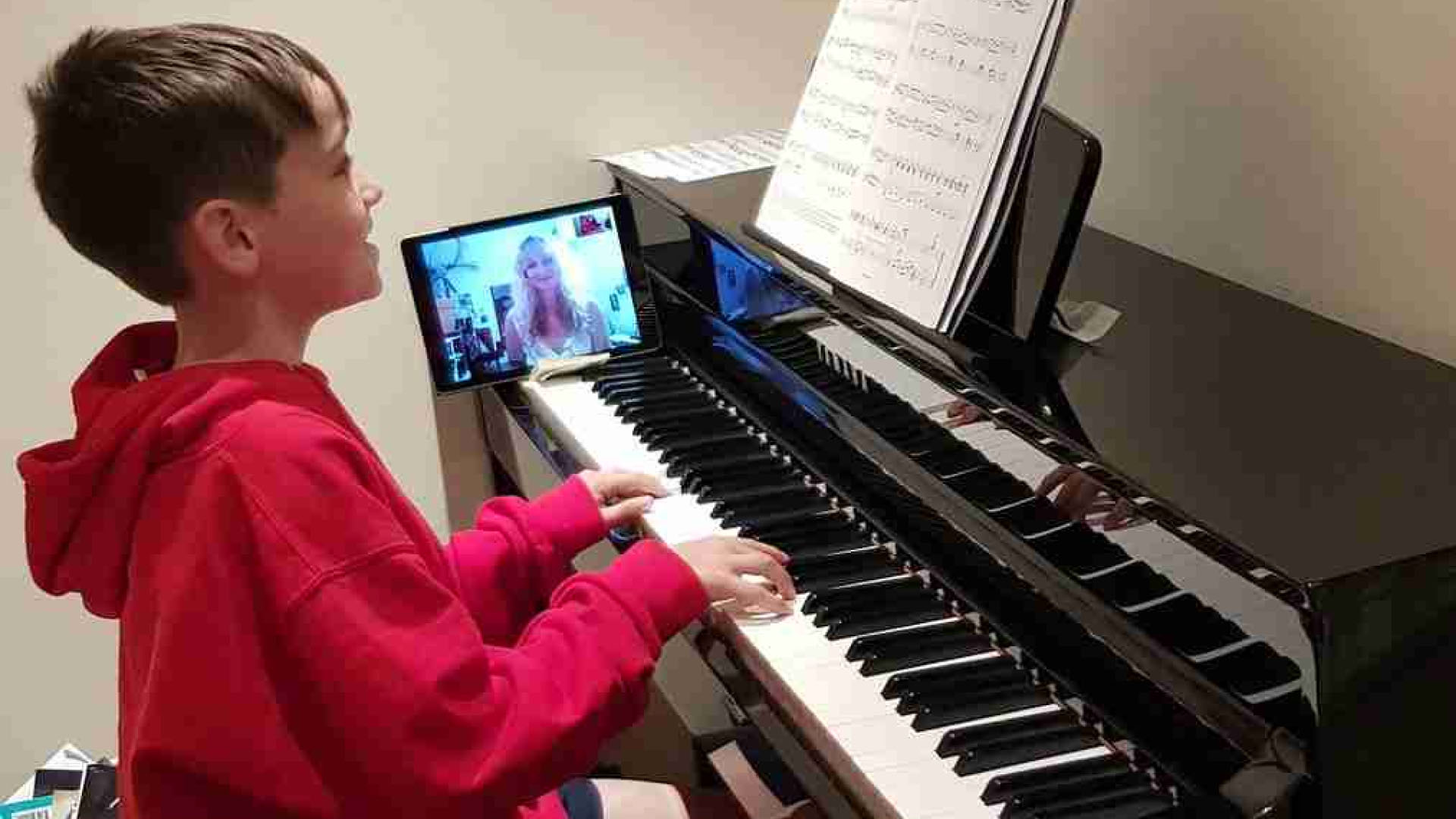 A child playing the digital piano with an online lesson on their phone